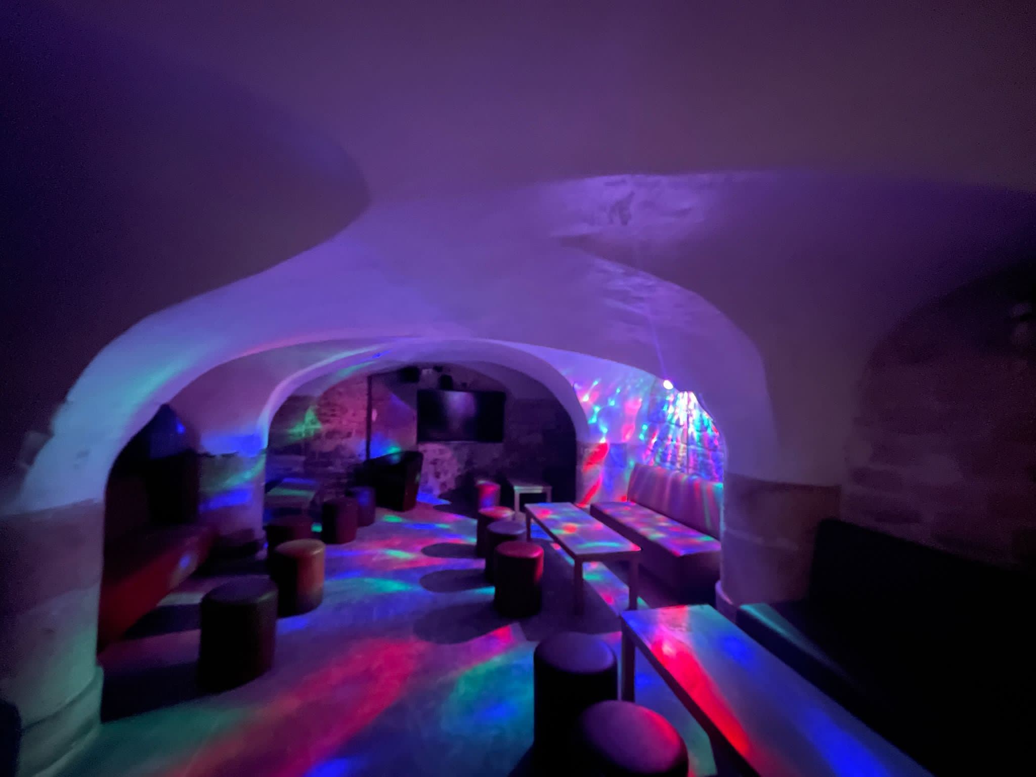 La cave voûtée de Ces Années Là : voûtes blanchies, poufs et tables basses sous des lumières de couleur